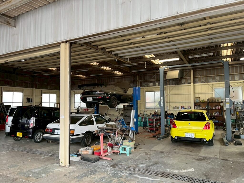 カーサービスオカダの整備工場内観。複数の車両とリフト設備が並ぶ、太田市の車検・修理・整備工場の作業場