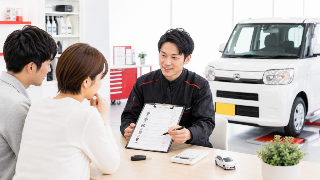 太田市で軽自動車の車検を検討する夫婦に、整備士が見積書を示しながら点検内容や整備費用を説明している様子