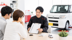太田市で軽自動車の車検を検討する夫婦に、整備士が見積書を示しながら点検内容や整備費用を説明している様子